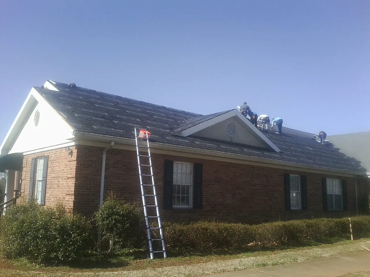 Crew tearing shingles off a brick ranch roof with a ladder set — Emergency Roof Repair work by our crew in Hempstead