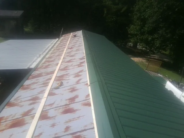 Old rusted panels beside newly installed green metal roofing — Wind Damage Roof Repair by Roofing Brothers in Hempstead