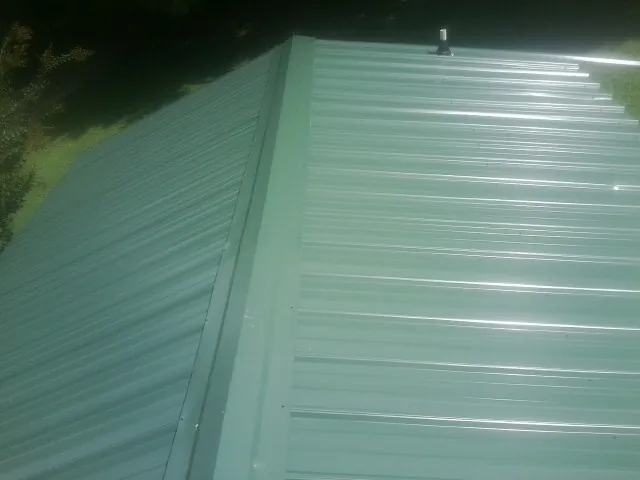 New green metal panels meeting at the ridge of a roof — Flat Roof Repair work by our crew in Hempstead
