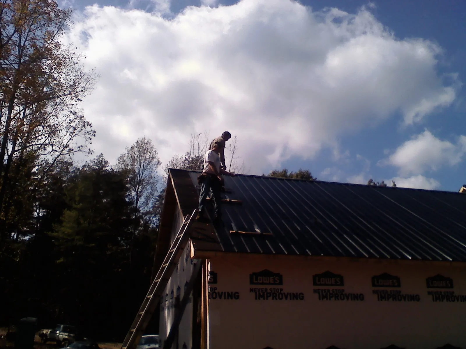 Roofer fastening dark metal panels high against a cloudy sky, from a Roof Inspection job in Hempstead